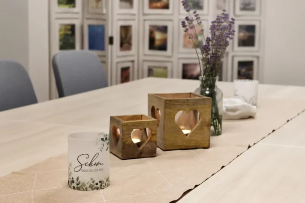 Tisch mit Kerzenhaltern in Herzform, Glasvase mit Lavendel und Teelichtern, dahinter Stühle und Bilderwand.